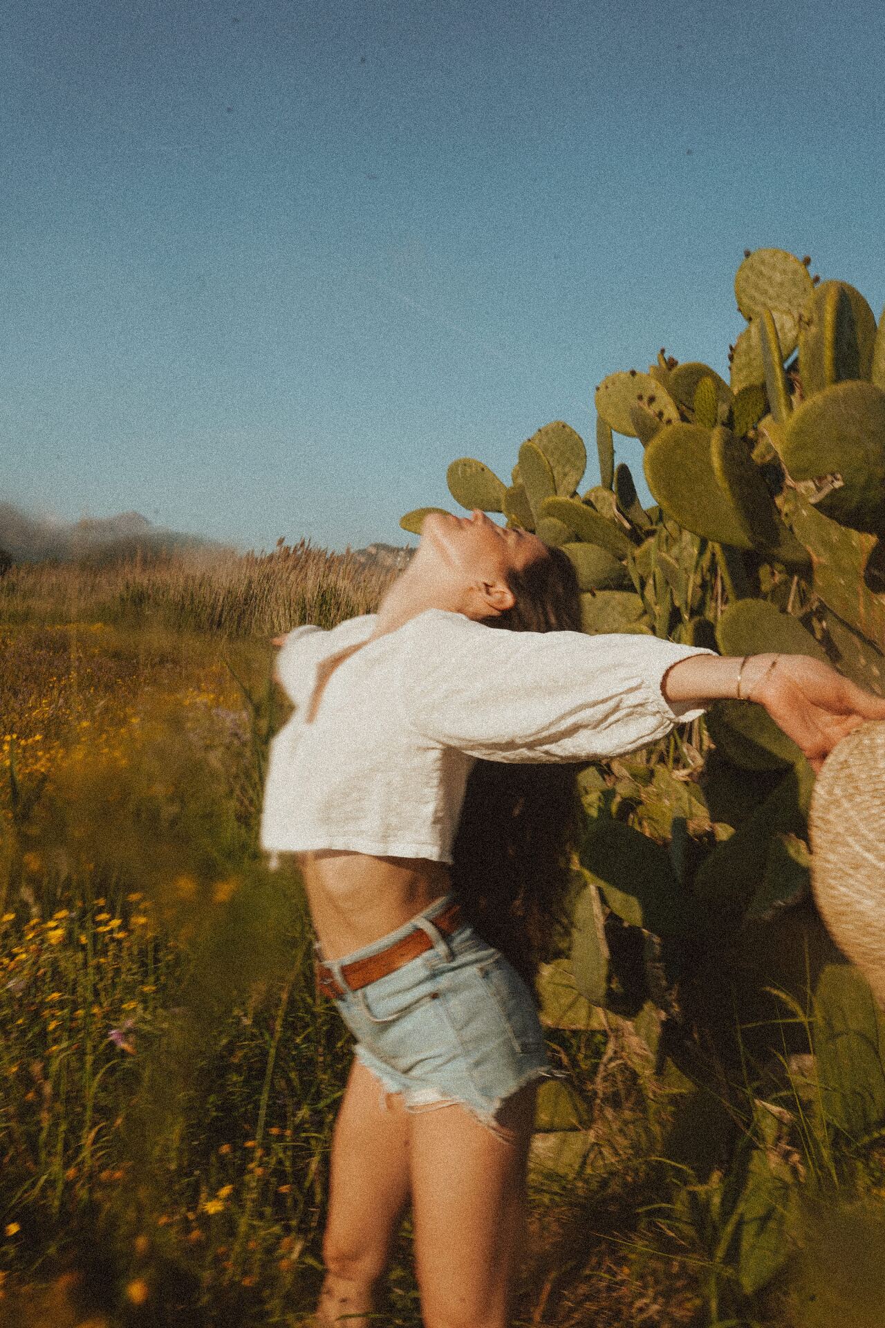 Woman in a sunlit wildflower field, arms open and head tilted toward the sky